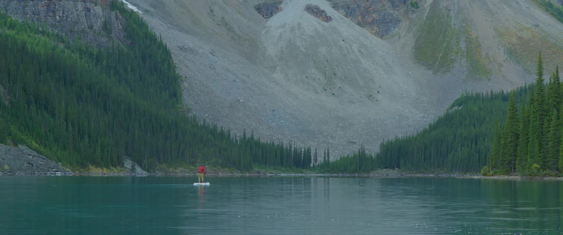 A person paddle boarding on a lake with trees and a mountain in the background