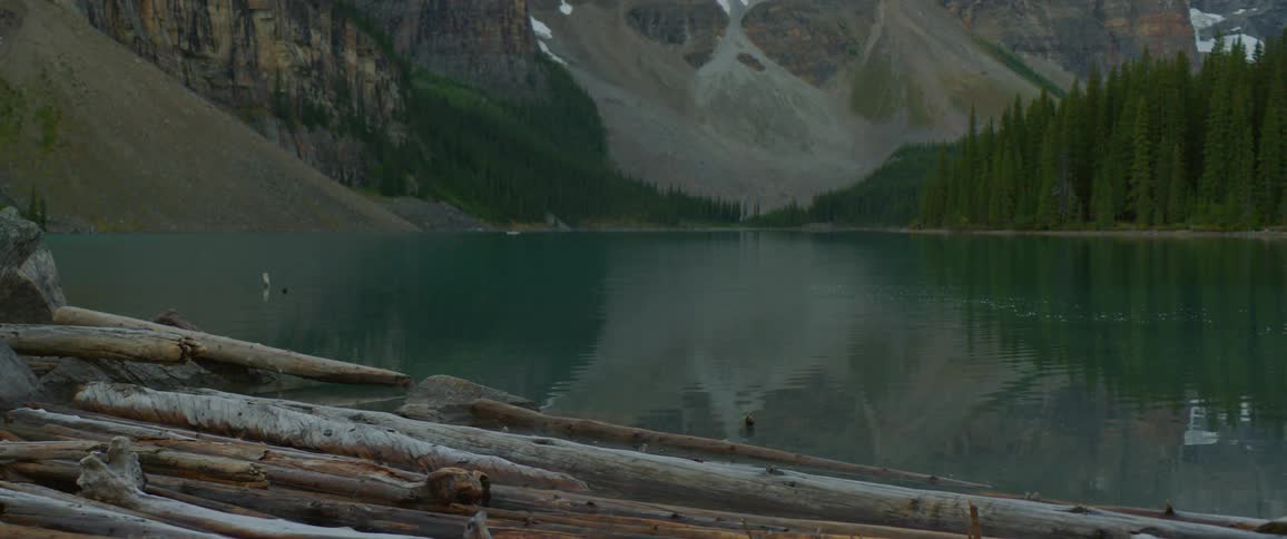 A blue green lake surrounded by forest and mountains during the day