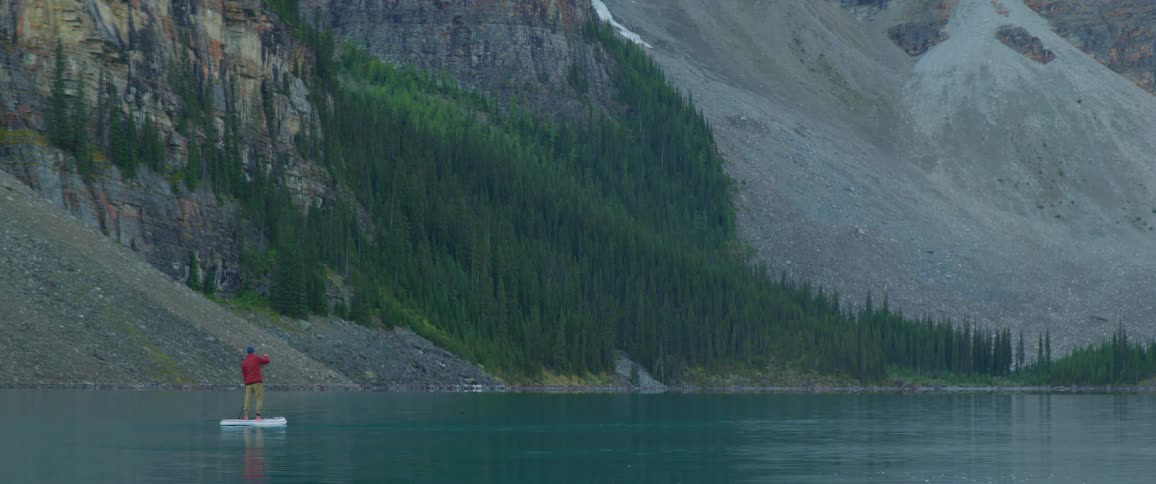 A person paddle boarding on a lake with trees and a mountain range in the background