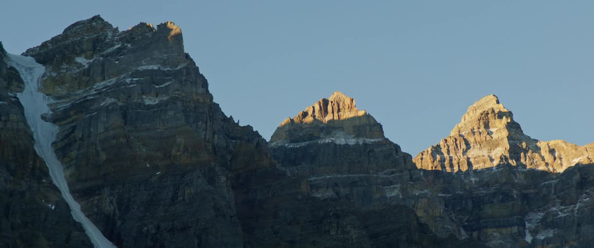 White snow on the rocky peaks of a mountain range at sunset