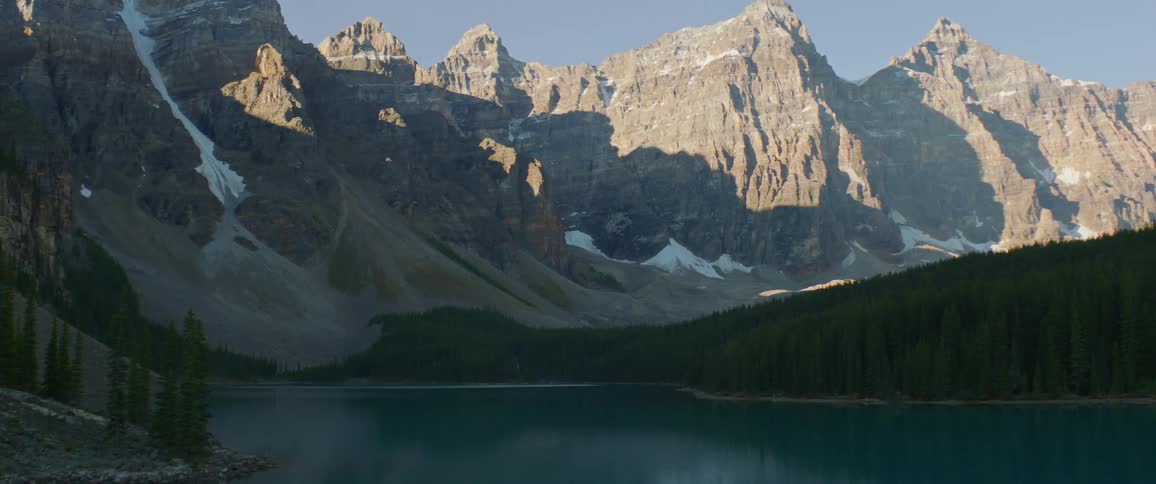 A lake in the shadow of a stone mountain ridge on a sunny day