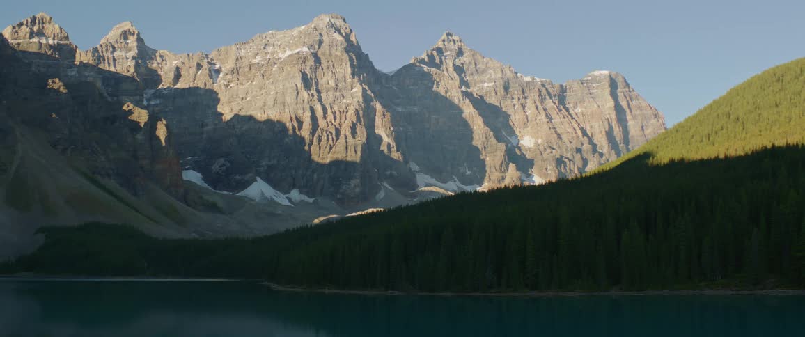 A steep stone mountain ridge and a hill covered in forest under a clear daytime sky