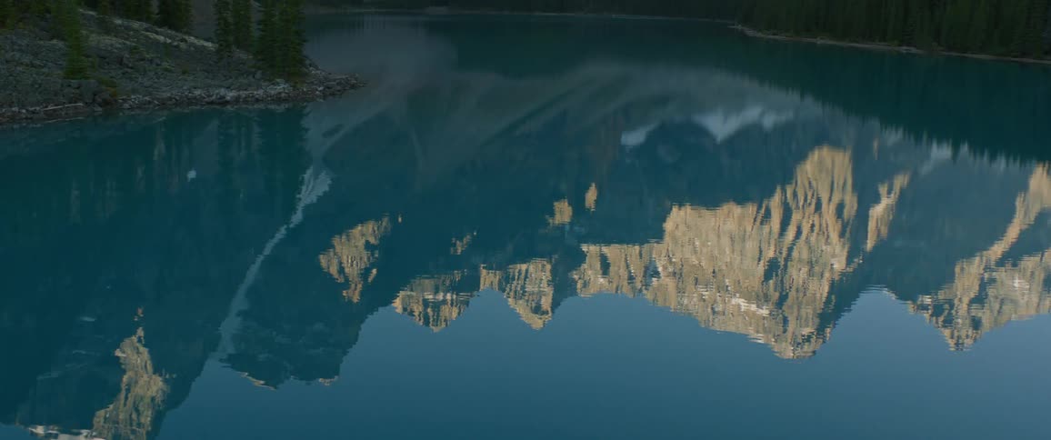 A lake reflects the barren stone mountain and deep blue sky above it