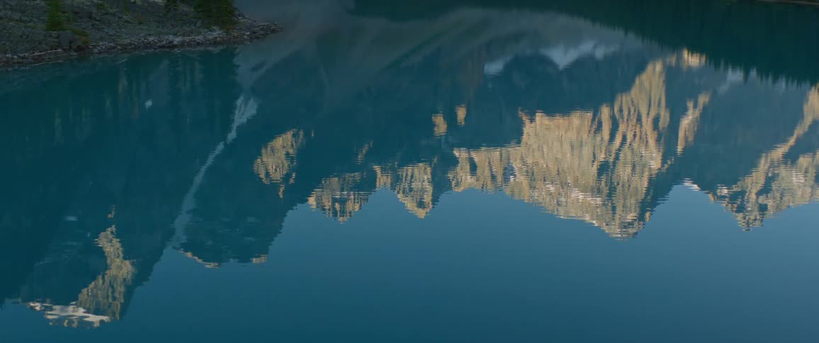 The surface of a lake reflecting a mountain ridge under a clear sky