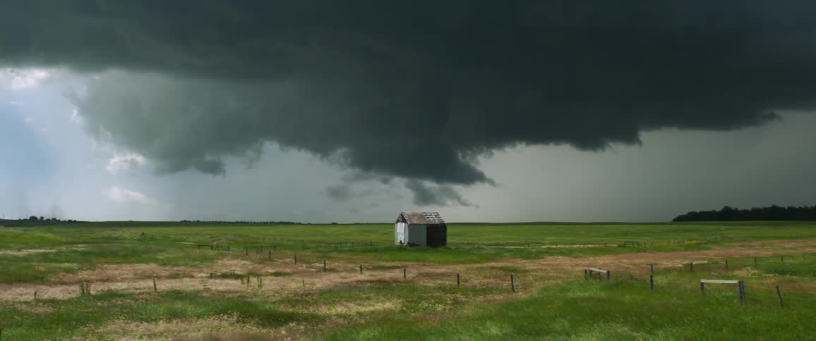 Dark clouds cover the sky over a small shed in a rural field