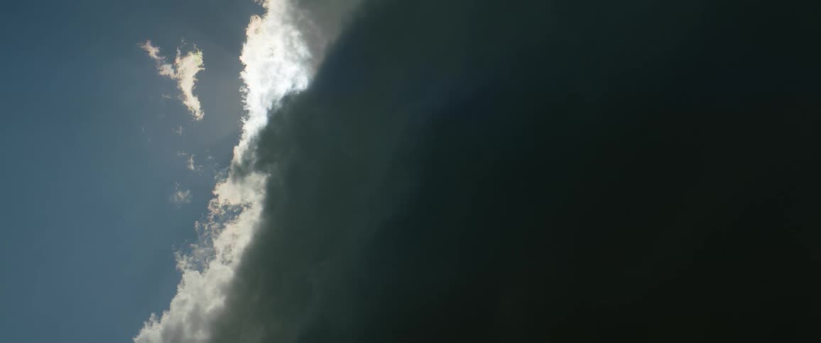 Camera pointing up to the sun hiding behind a big dark storm cloud