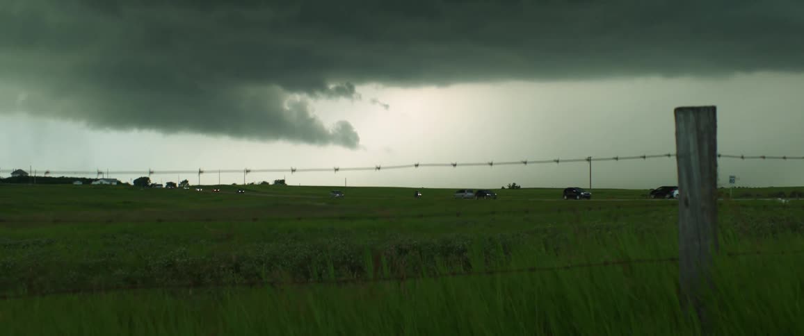 Cars driving beneath dark storm clouds on a rural road