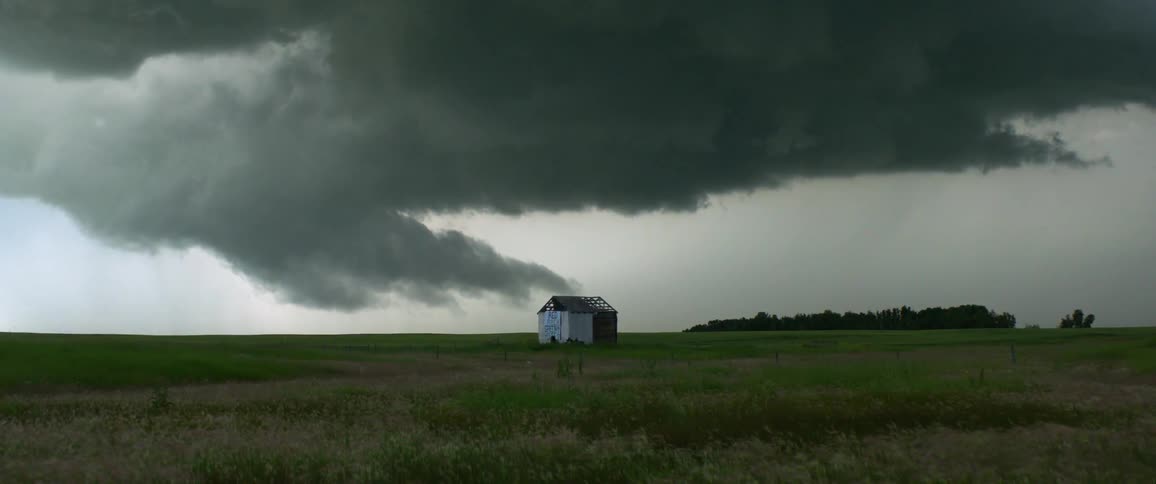 Dark clouds loom over a half built shack in a grassland in the evening