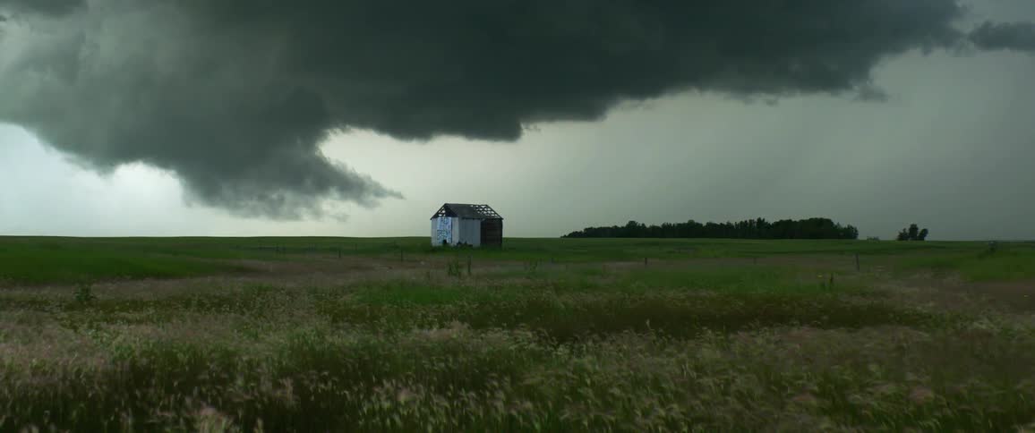 An abandoned shack in a grass field under storm clouds on an overcast day