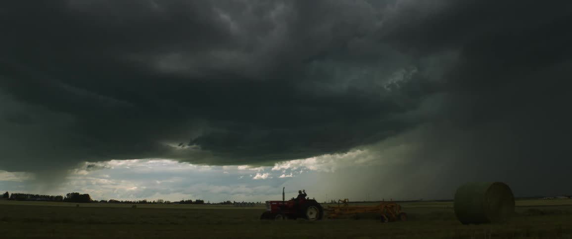 Thick dark storm clouds pouring rain down farm land plains