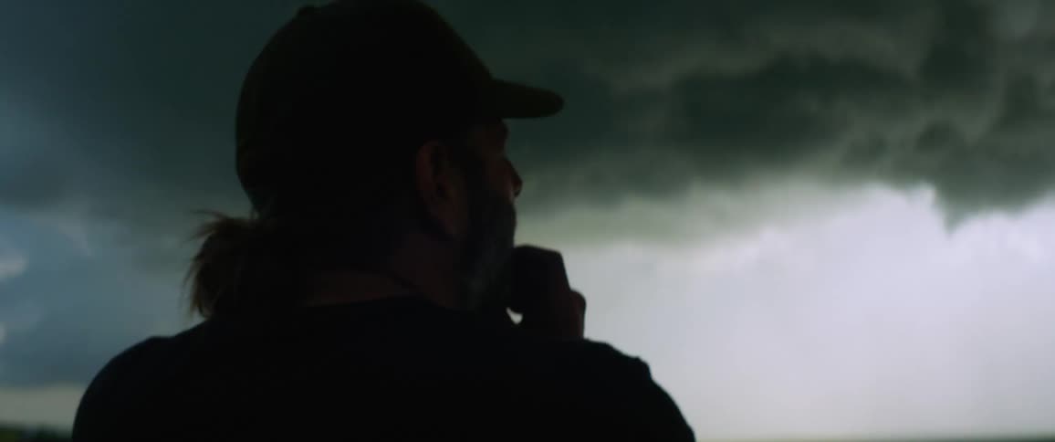 A man stands taking a photo of an approaching storm in the countryside