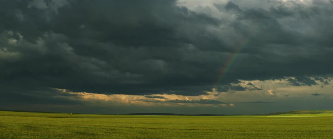 A rainbow and dark storm clouds over a grass field