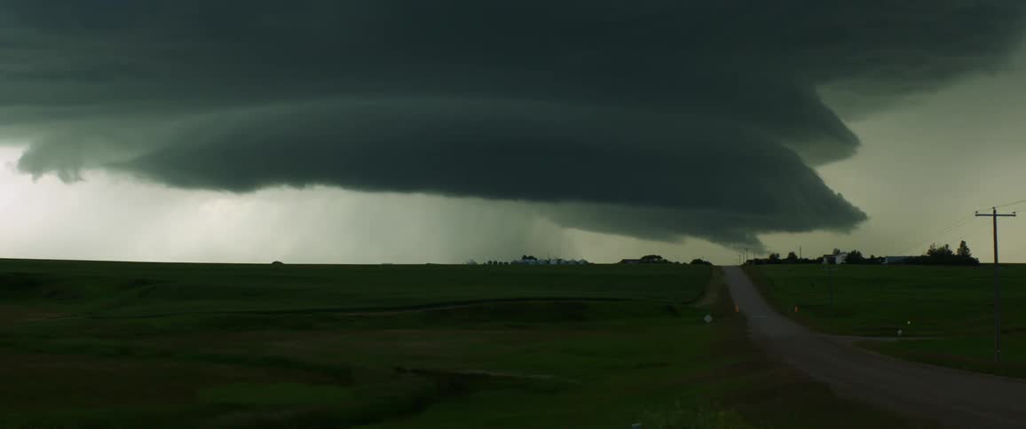 Thick dark mushroom like clouds loom over a countryside in the evening