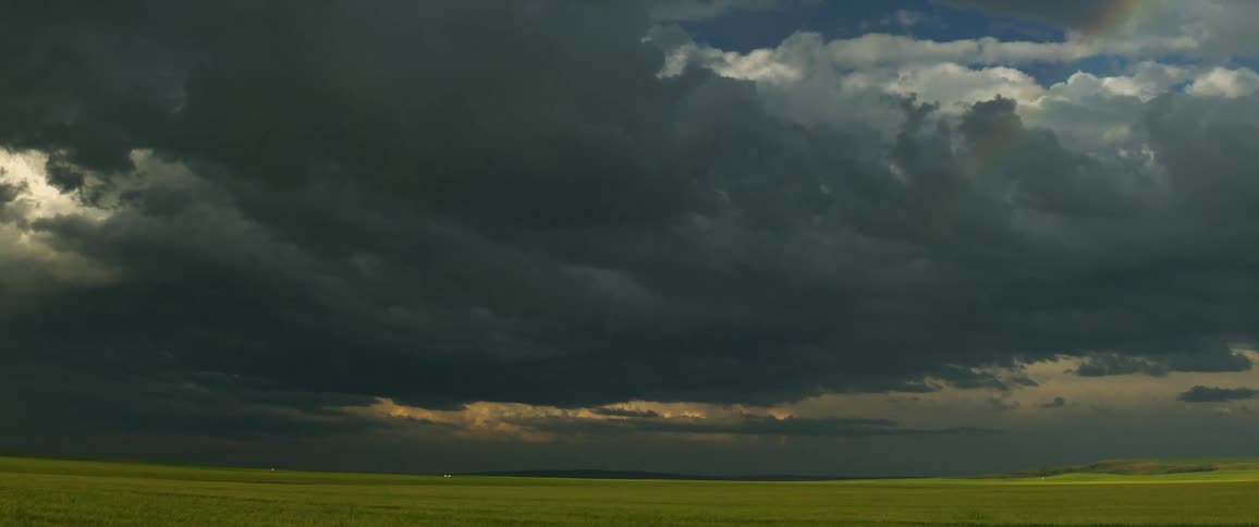 Dense clouds sit above a vast green field in the countryside