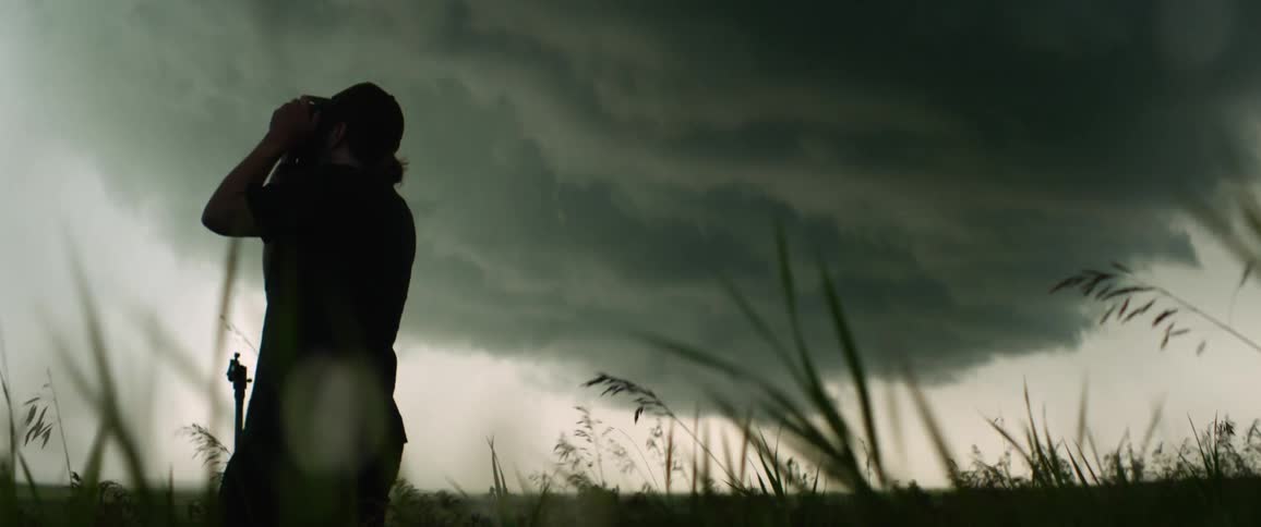 Silhouette of a man taking pictures of storm clouds in a field