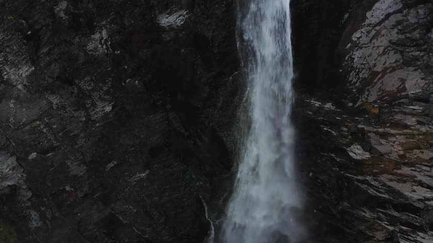 Flurries float around waterfall flowing down sheer wet cliff