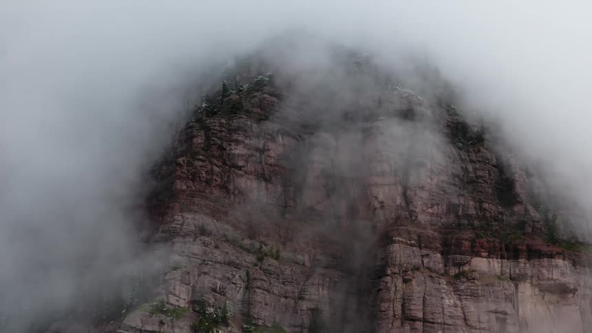White clouds cover the steep cliffside of a mountain