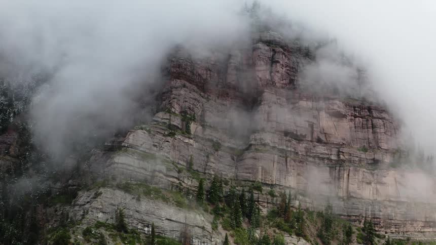 White clouds cover the steep cliffs of a mountain side
