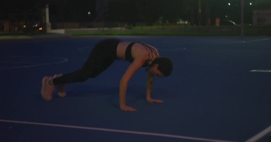 Young fit woman wearing sports clothing exercises on a park in the city at night