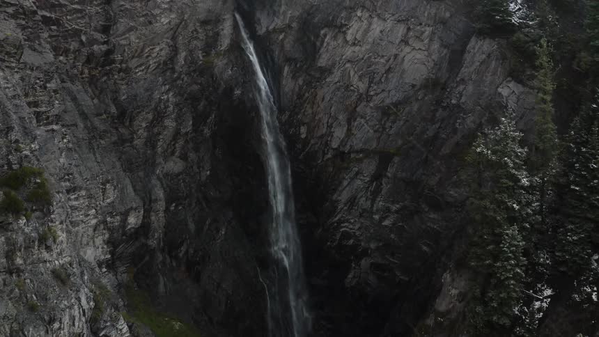Aerial view of snow falling as a waterfall crashes down a canyon in to the river below
