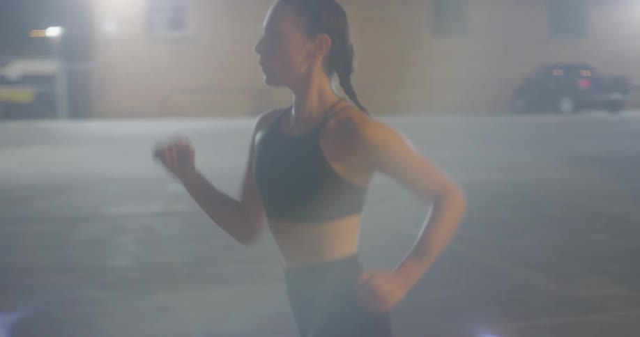 A young woman exercises by running along a city street at nighttime