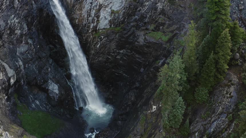 Within forest covered mountains is a waterfall that is splashing down into a small lake below