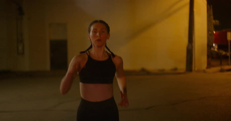 A woman in a black sports bra jogging alone on a city street at night