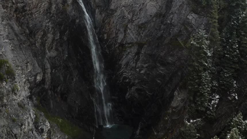 Water falls into a ravine in the mountains as heavy snow falls from the sky