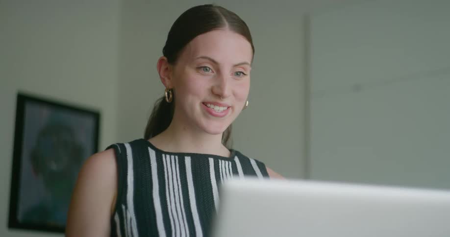 Woman stands next to wall with framed art having video call on a computer