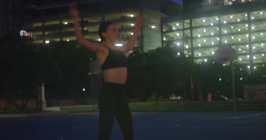 A woman is doing jumping jacks on a basketball court at night