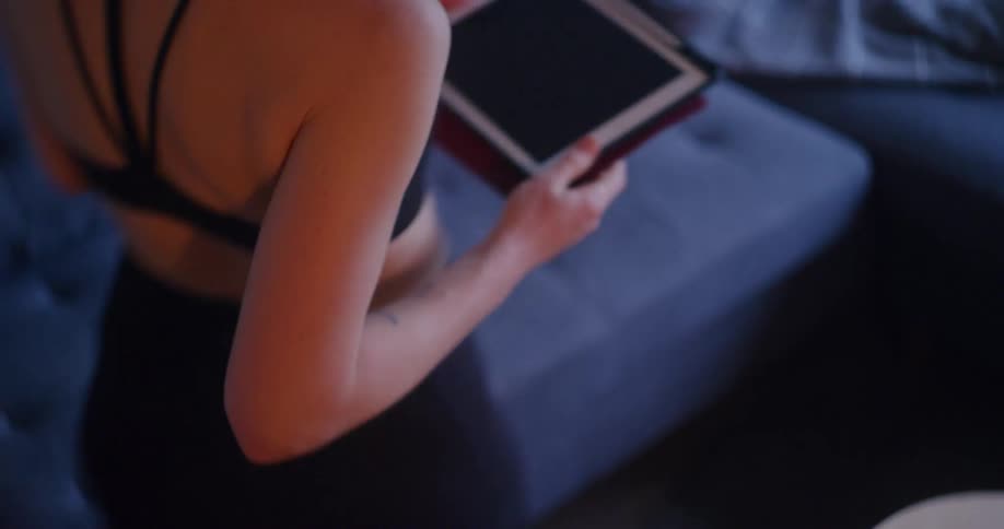 A young woman picks up a tablet from a table at home and sits on a couch