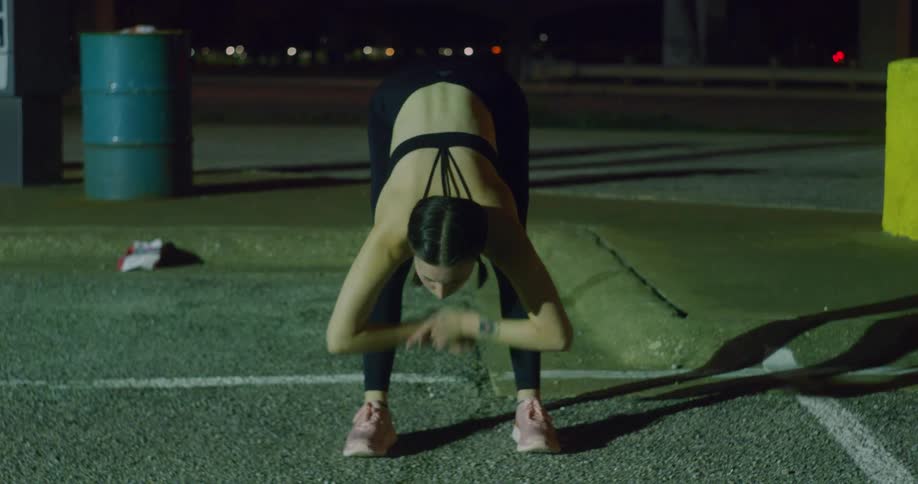 Young fit woman in sports clothes stretches on the street of a city at night