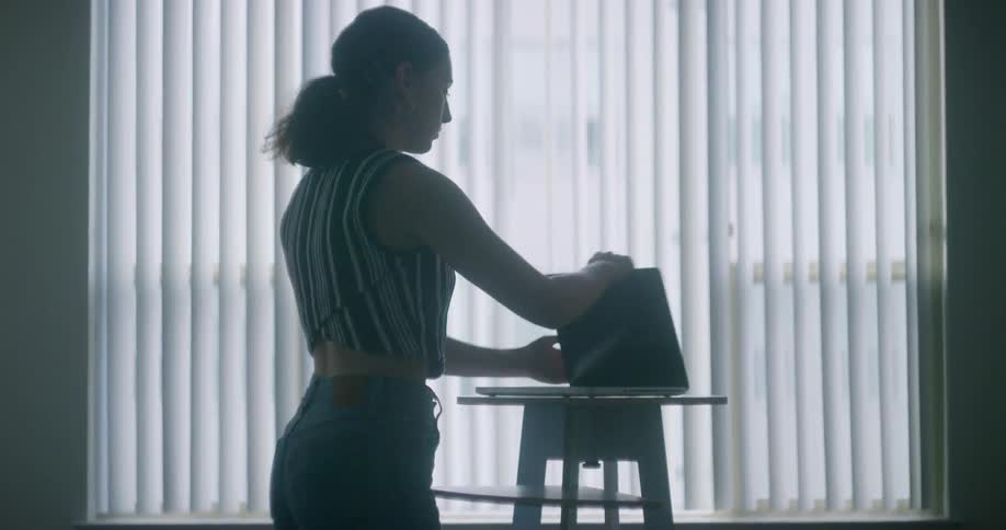 A woman places a laptop on a stool and opens it up