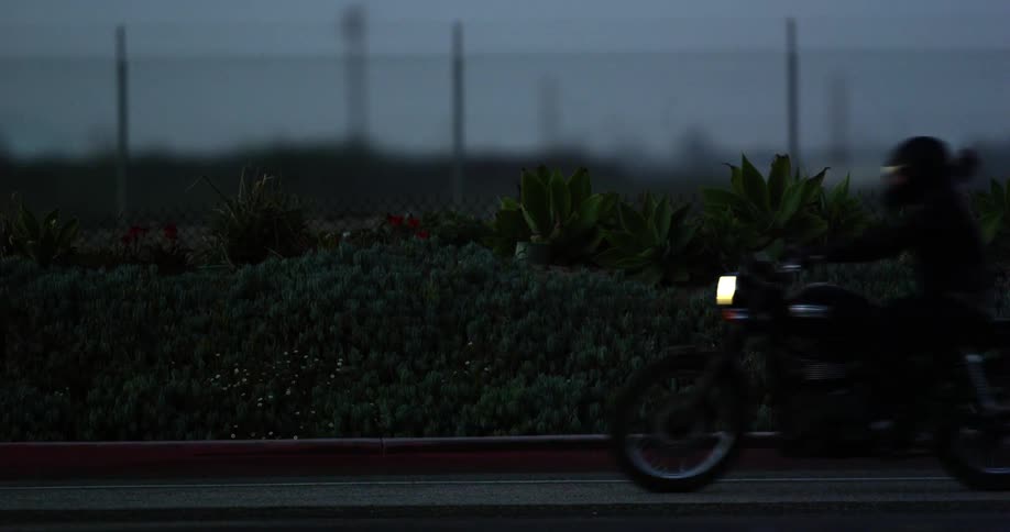 A person riding a motorcycle passes on the road in front of a fence with grass