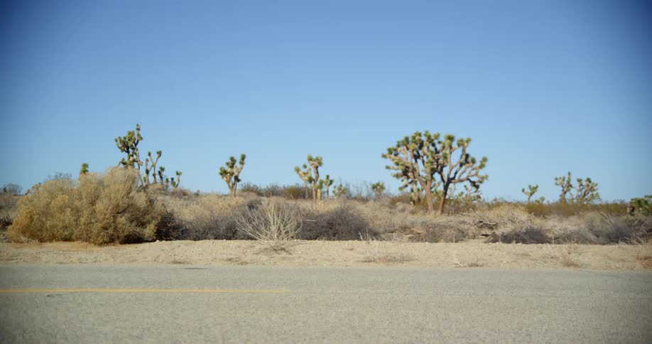 A person with a helmet riding a motorcycle on a road in the desert with the sky and clouds in the background
