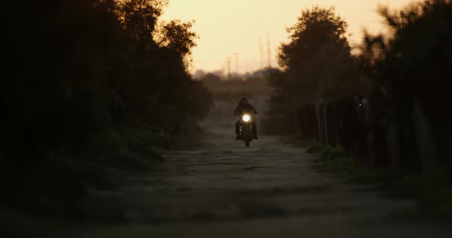 A motorcyclist riding on a rural road at sunset