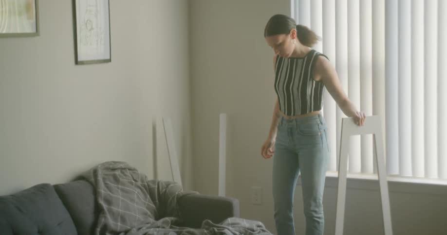 Young woman enters the living room to pick up and assemble a stand