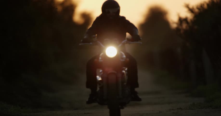 A motorcyclist riding on a dirt path with an orange sky at sunset