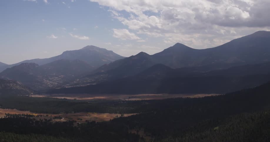 A valley and mountains sit under a partly cloudy blue sky