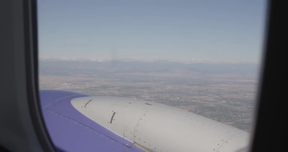 The wing of a plane is seen from a window inside the plane as it flies