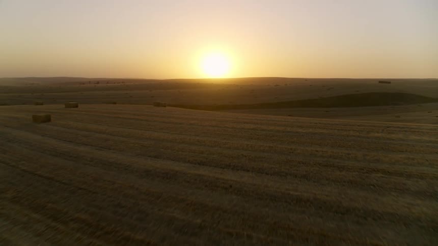 Skimming over freshly harvested hay bales as the sun hangs low in the sky over sprawling farmland
