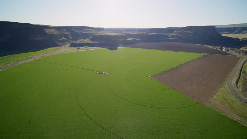 Pullback reveal of a semicircle green crop field in a canyon valley