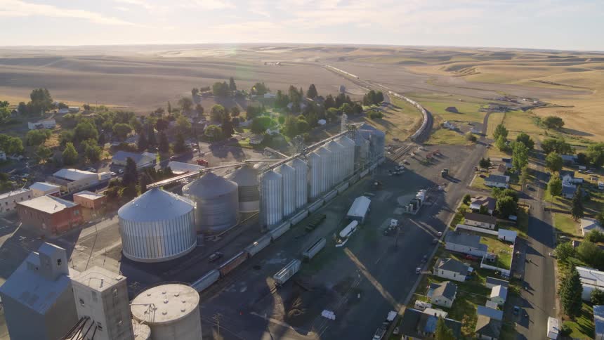 Wide overview of a grain storage facility in a small farming community surrounded by farmland and rolling hills