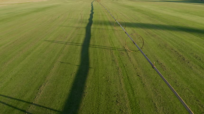Flying above a rolling irrigation system casting long shadows along a green field at sunrise