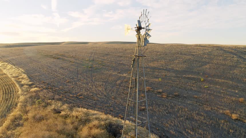 Orbiting descent around a windmill between two farm fields as the sun rises on a beautiful morning