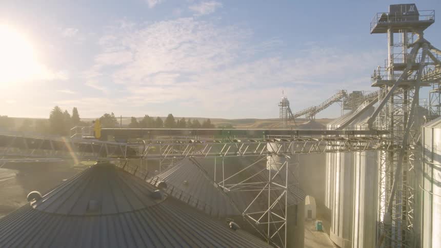 Flying thru the silos and tanks of a modern grain handling facility surrounded by a small town and rolling hills