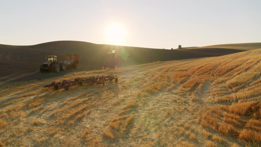 Sunrise pullback reveal of a parked tractor and plow equipment near a storage shed along rolling farmland
