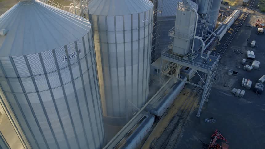 Sunrise ascent over a grain storage facility filling rail cars with barley