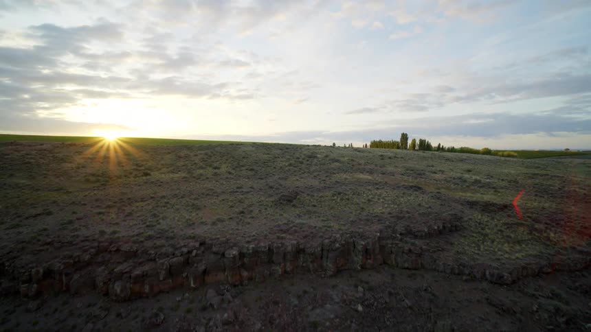 Flying over a barren cliff to reveal green crops growing in fertile soil as the sun rises in the distance