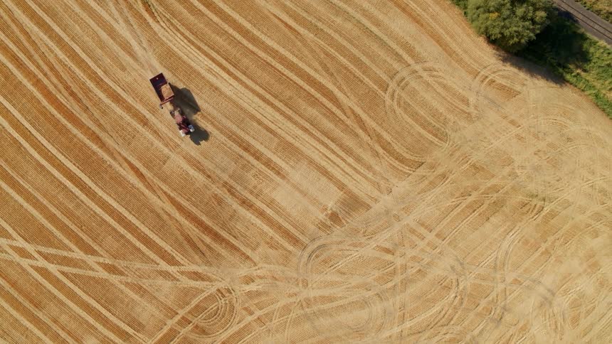 A birds eye view of a red tractor pulling a grain cart along a harvested wheat field